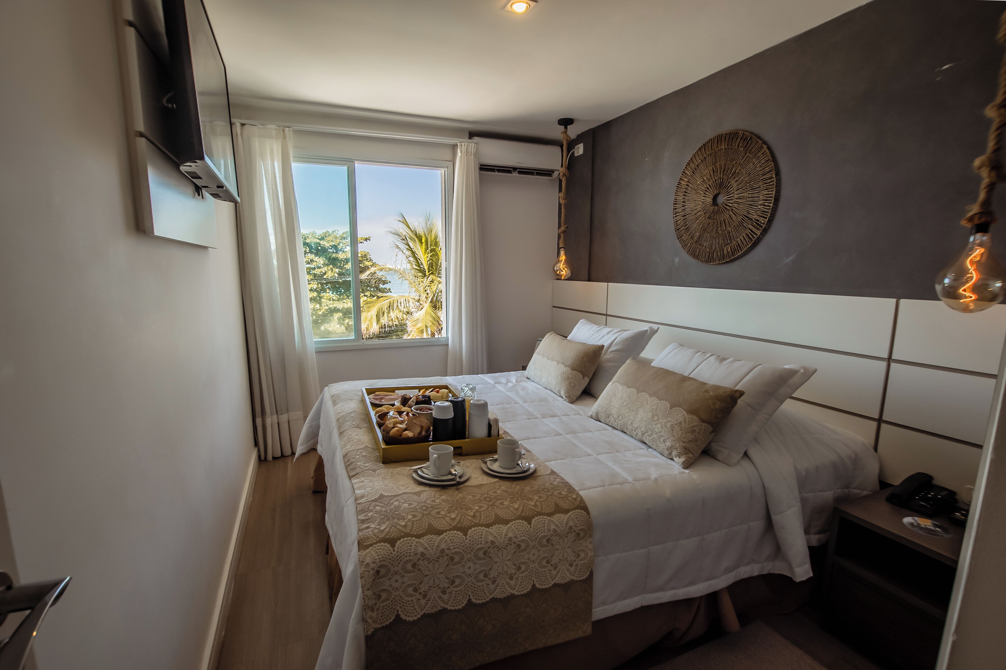 Een hotelkamer met een groot bed, een nachtkastje, gordijnen voor het raam en uitzicht op palmbomen.
