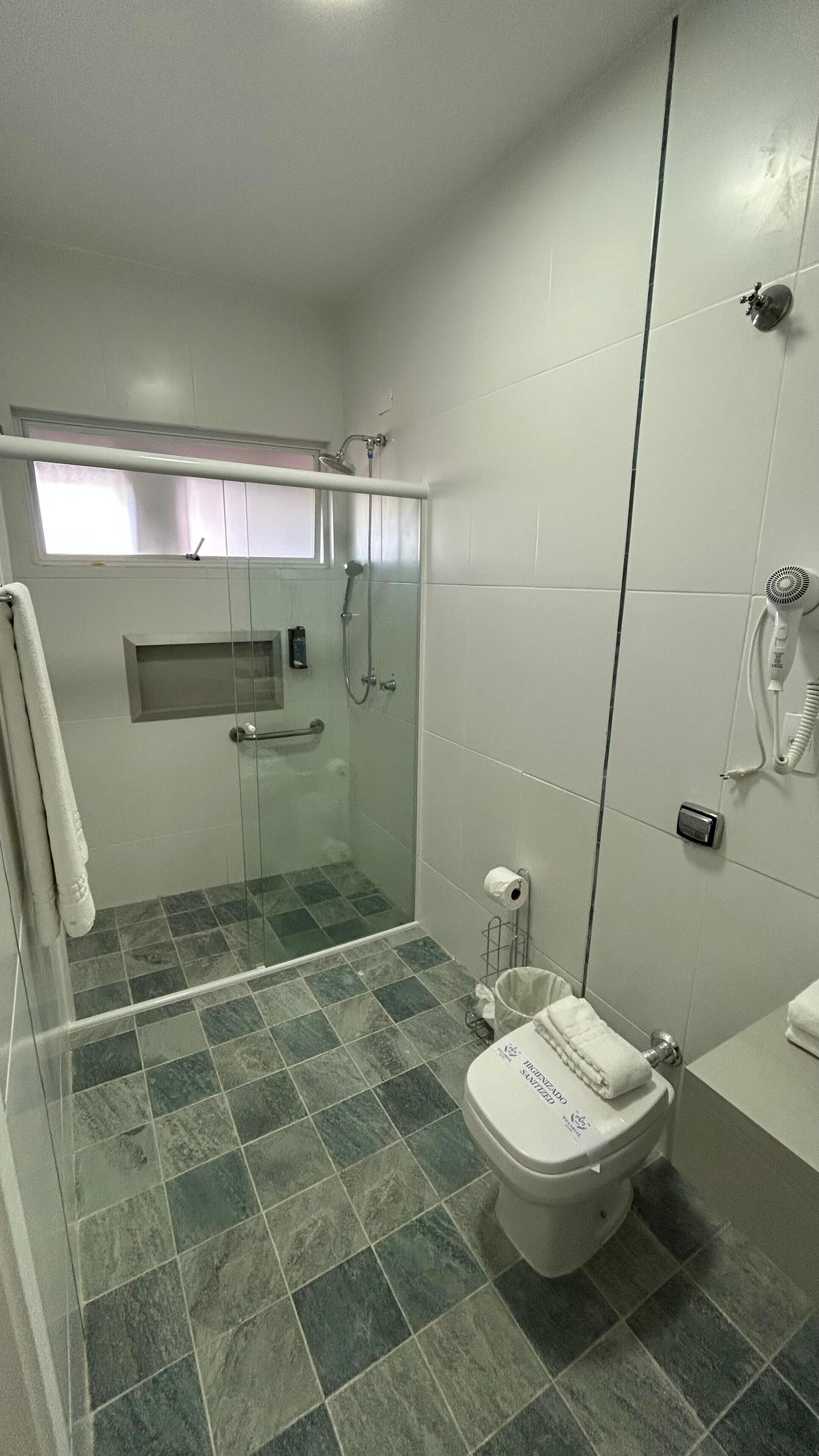 Un baño moderno con ducha envuelta en vidrio, inodoro con tapa y perchero para toallas.