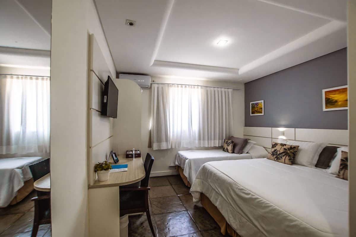 Une chambre d’hôtel avec deux lits, un bureau avec une chaise, une télévision et une fenêtre avec des rideaux.