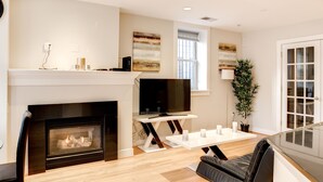 A modern living room with a fireplace, a flat-screen TV, a dining table, and a large potted plant. - Fully Furnished Apartment in Washington near Logan Circle (Washington)