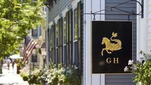 A black sign with a golden horse logo and the letters "GH" hanging from a building's awning. - Greydon House (Nantucket)