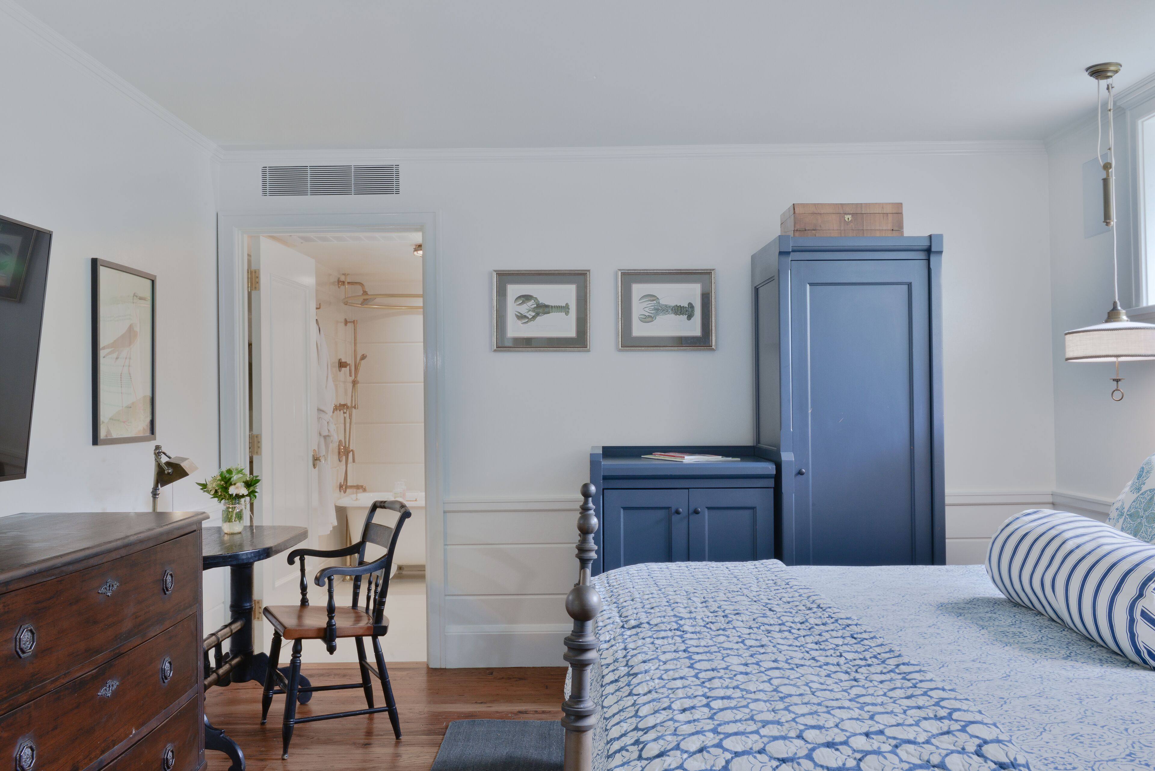 Ein Schlafzimmer mit Bett, Kommode und Schreibtisch mit Stuhl. An der Wand hängen zwei gerahmte Bilder.