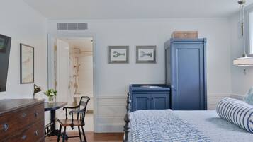 A bedroom with a bed, dresser, and a desk with a chair. There are two framed pictures on the wall.