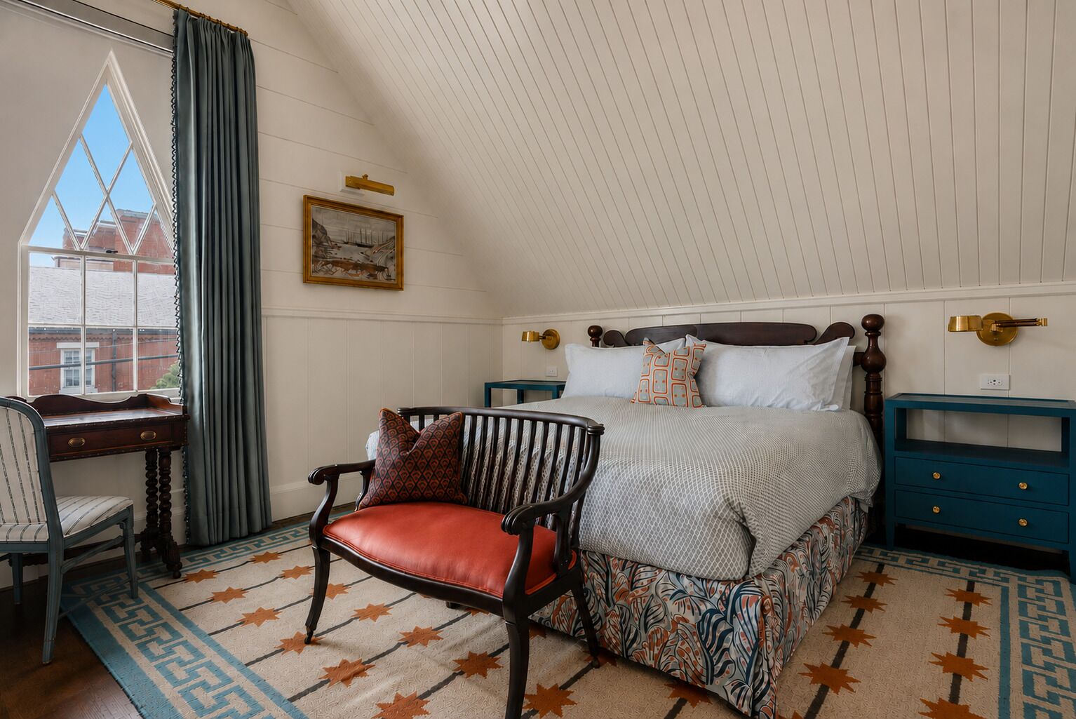 A bedroom with a bed, a chair, a desk, and a nightstand.