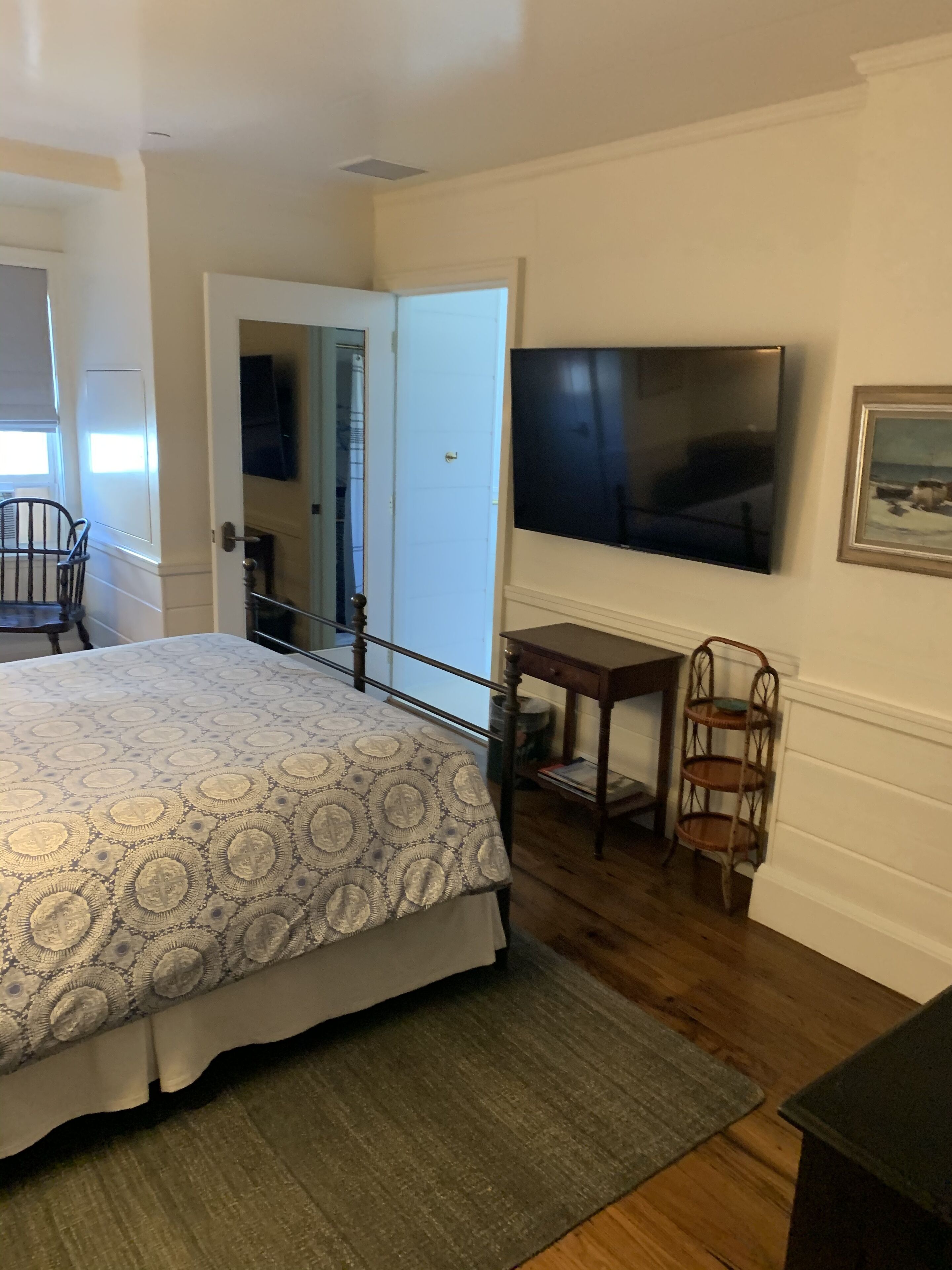 Un dormitorio con cama, televisor en la pared, una mesita y una silla.