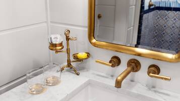 Un baño con lavamanos de mármol blanco, grifería dorada y espejo con marco dorado.