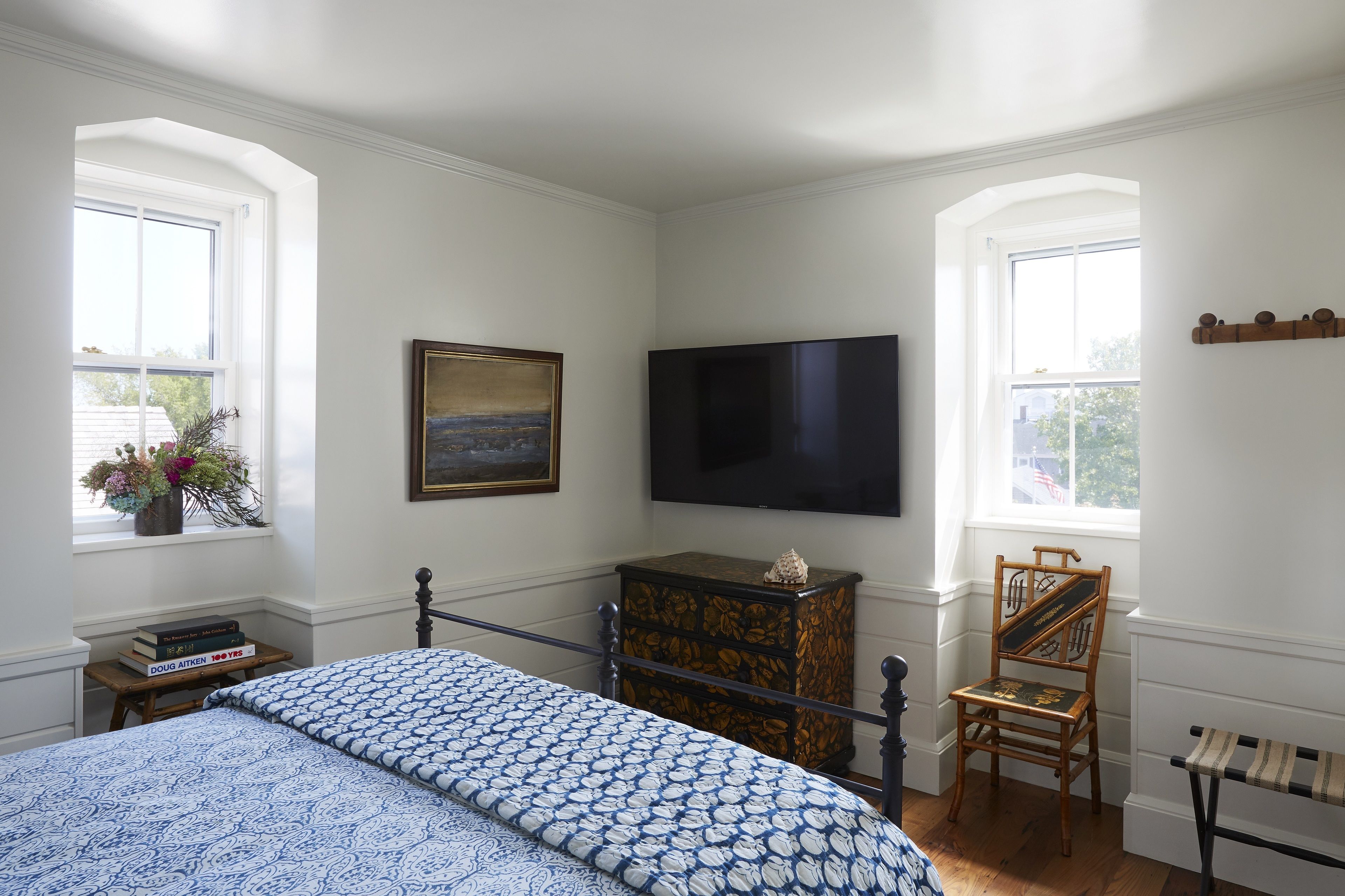 Une chambre à coucher avec un lit, une commode, une chaise, une télévision et des fenêtres.