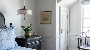 Quarto com cama, mesa de cabeceira, luminária, quadro emoldurado, porta e cadeira.