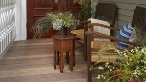 A wooden front door with decorative glass panels, a porch with a wooden table and chairs, and two hanging lanterns. - Greydon House (Nantucket)