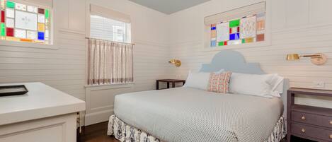 A bedroom with a bed, bedside tables, a dresser, a window with curtains, and a chandelier.