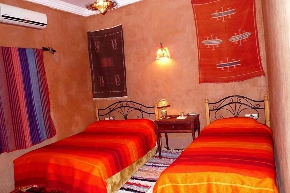 A room with two beds, a wall-mounted air conditioner, a lamp, and a tapestry.