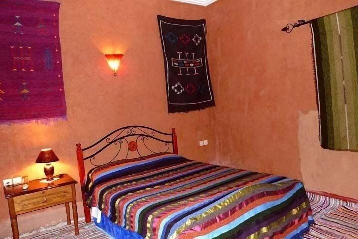 A bedroom with a bed, a nightstand, a wall-mounted lamp, and a tapestry.
