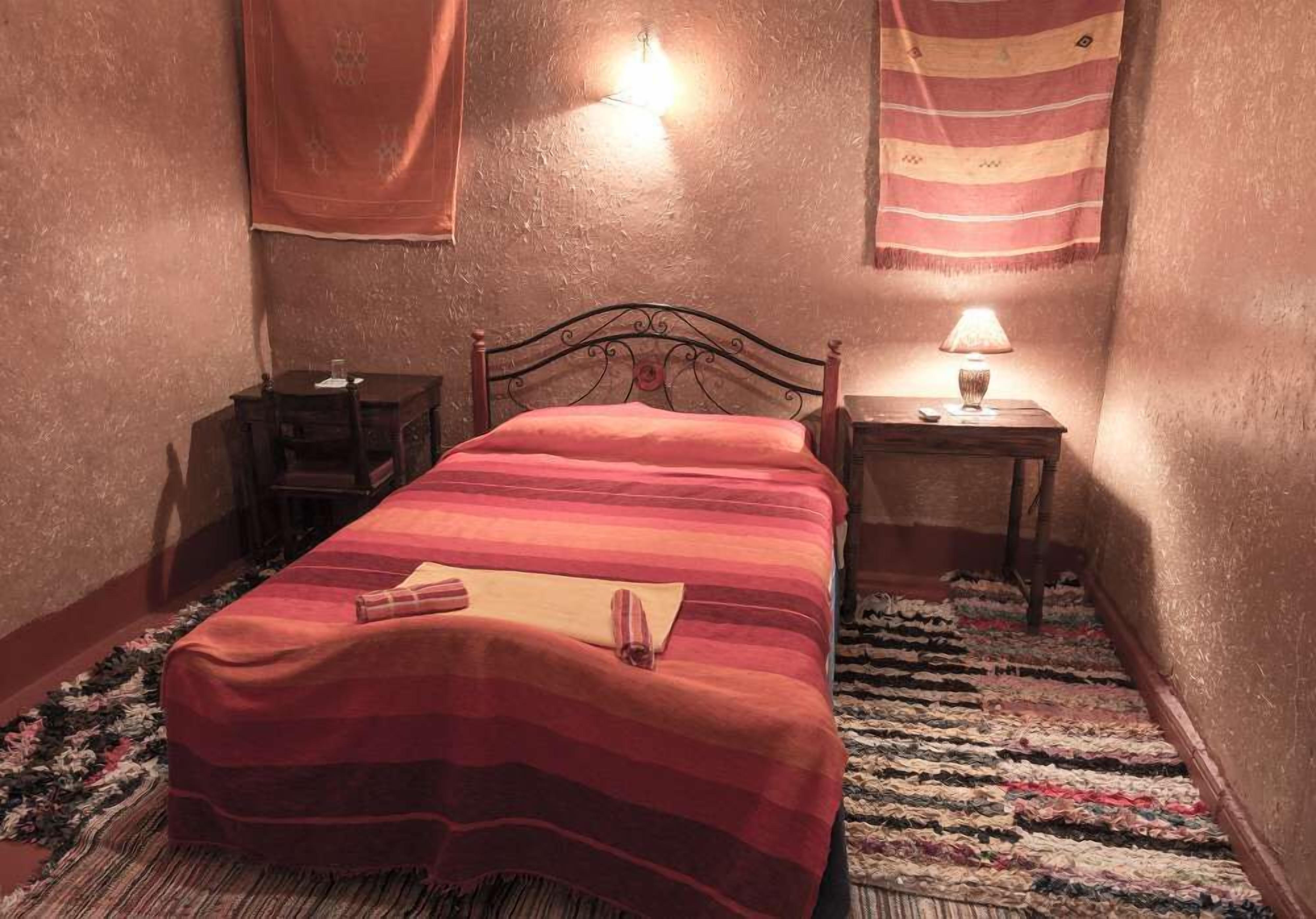 A bedroom with a bed, a nightstand, a lamp, and a wall-mounted light fixture.