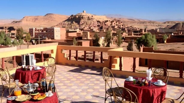 Una terraza con mesas dispuestas para comer, con vistas a un paisaje desértico que incluye edificios y montañas.