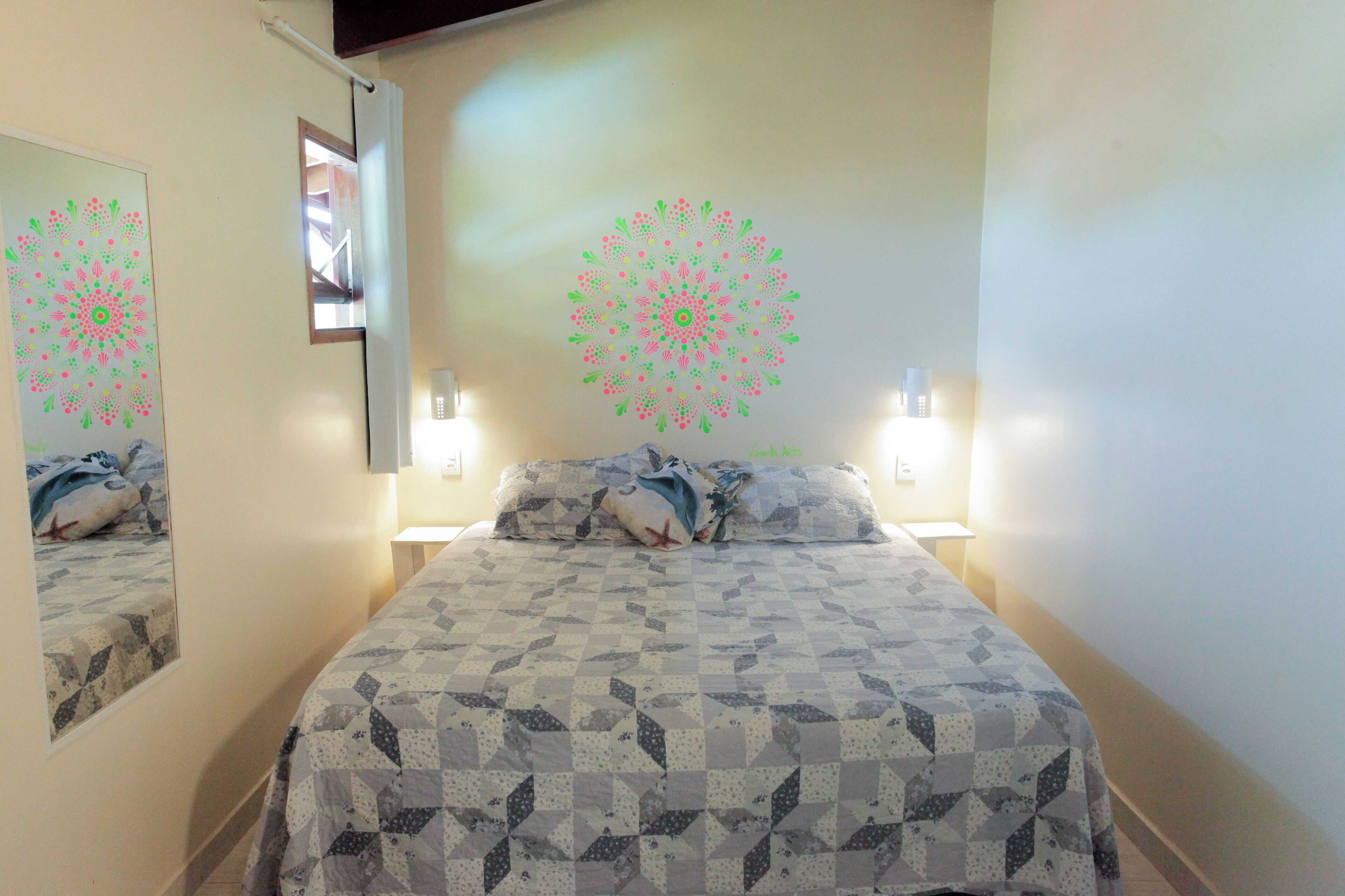 A bedroom with a bed, two bedside tables, a mirror, and decorative wall art.