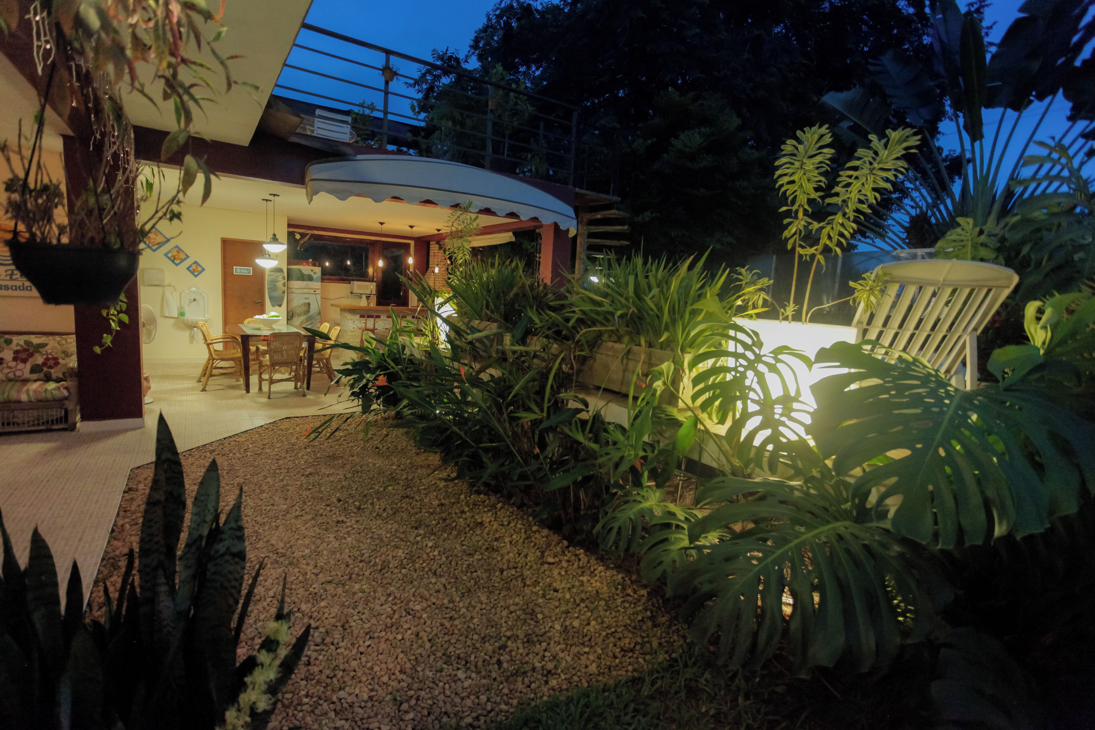 A well-lit outdoor area with a dining table and chairs, surrounded by various plants and a small garden.