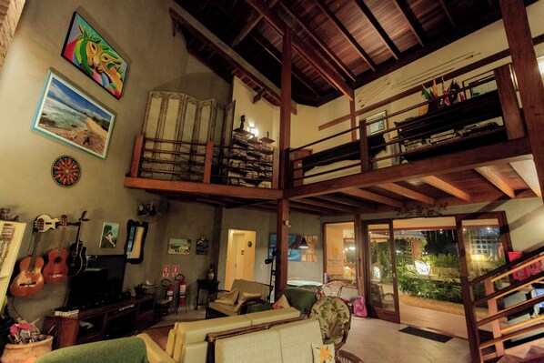 A spacious living area with a high ceiling, wooden beams, a television, guitars, and a dartboard. - Ubatuba Ecologic Pousada (Ubatuba)