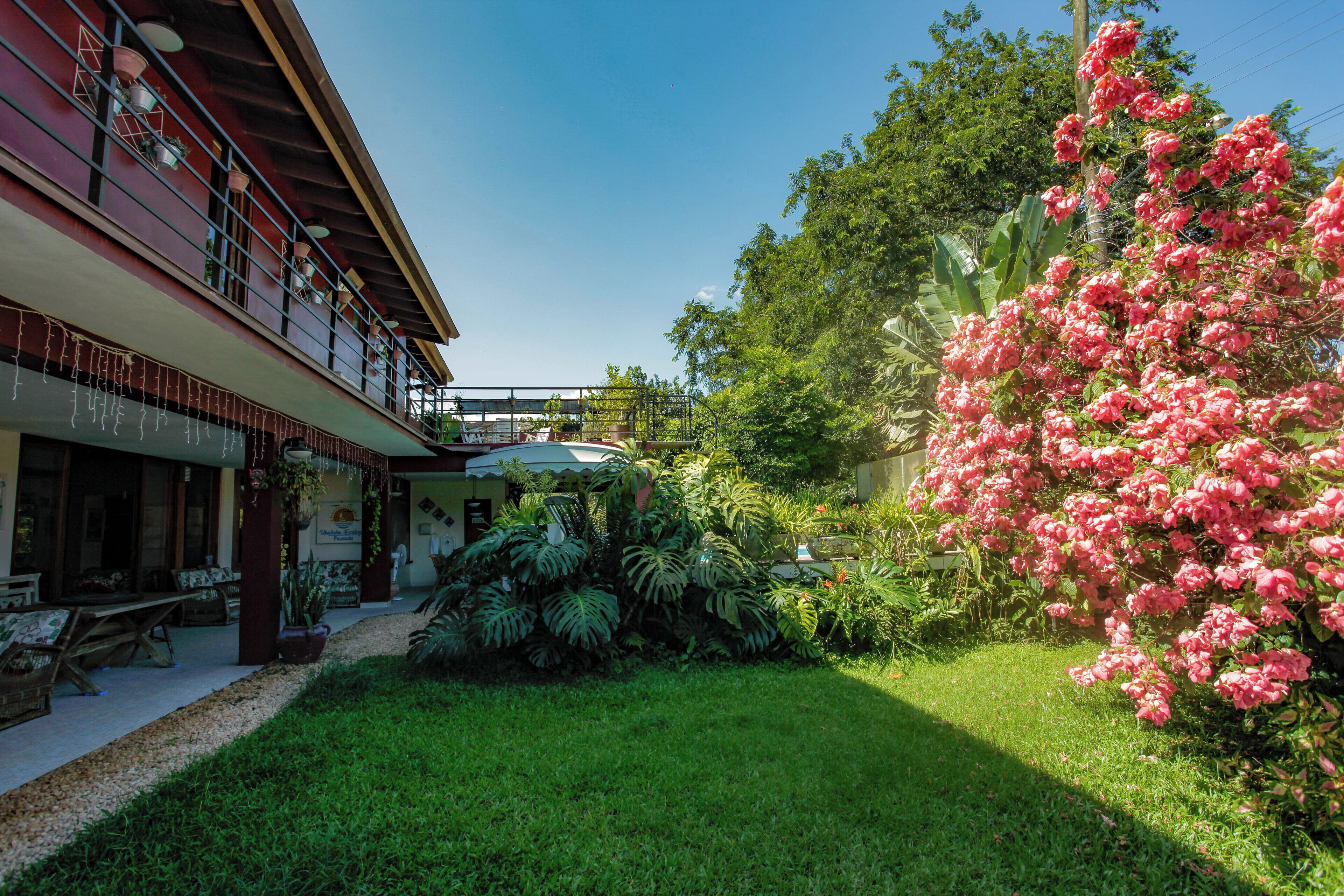 Um hotel com área de estar coberta ao ar livre, um jardim com diversas plantas e uma varanda com plantas pendentes.