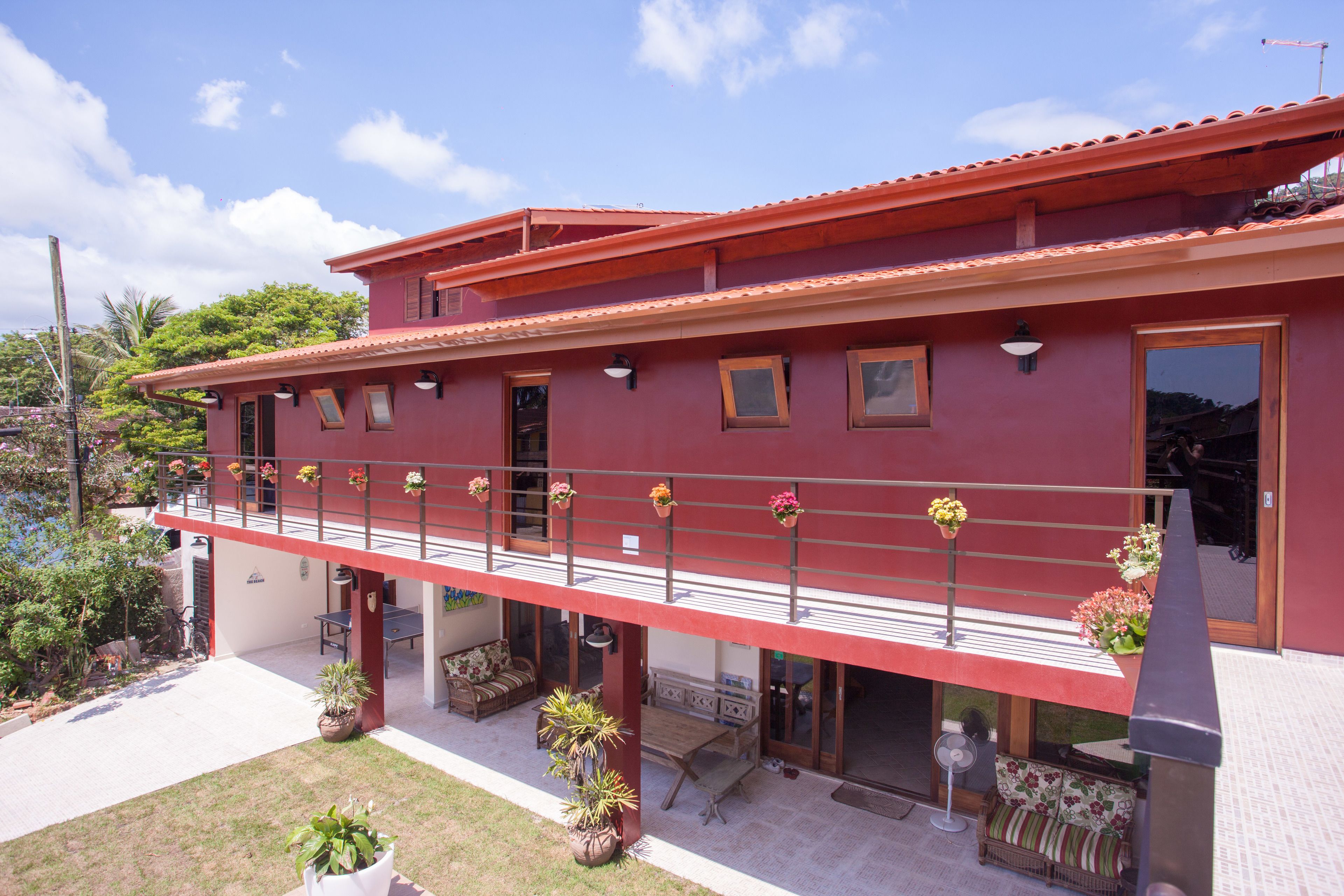 A red two-story building with a balcony, potted plants, and a patio area.