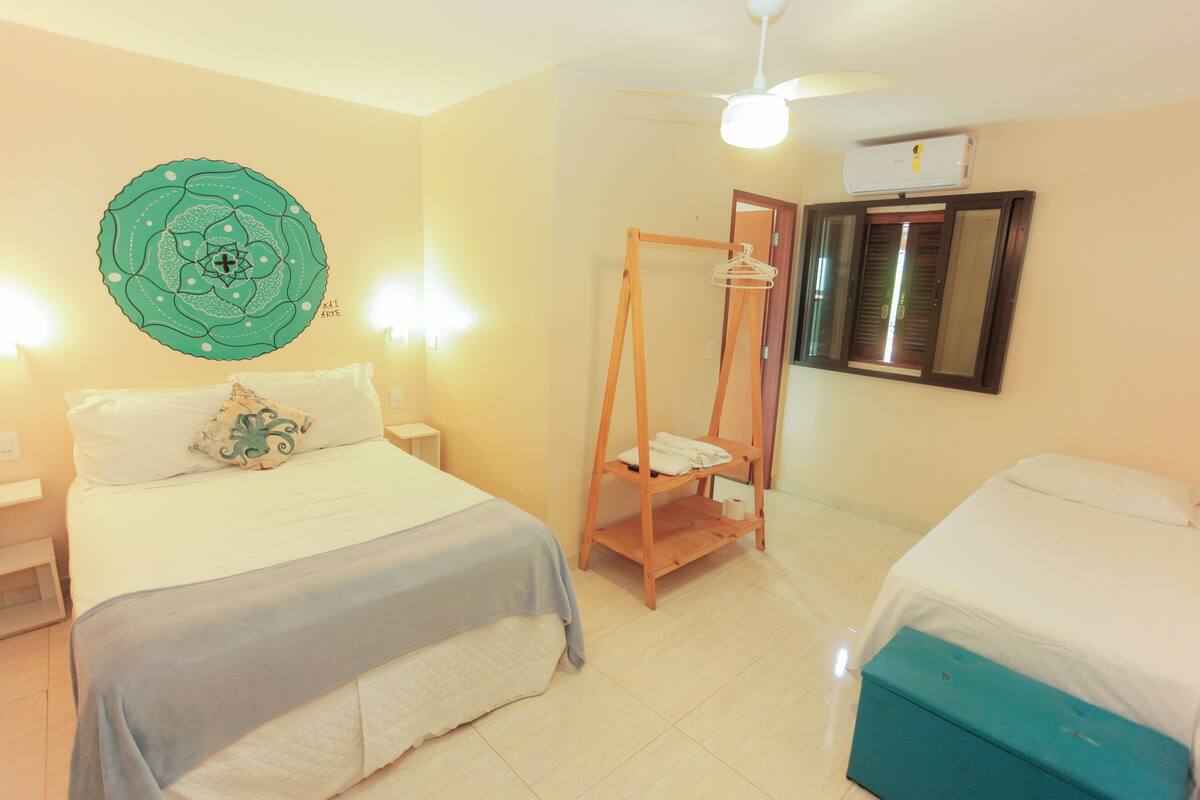 A hotel room with a bed, a hanging clothes rack, a ceiling fan, and a window with blinds.