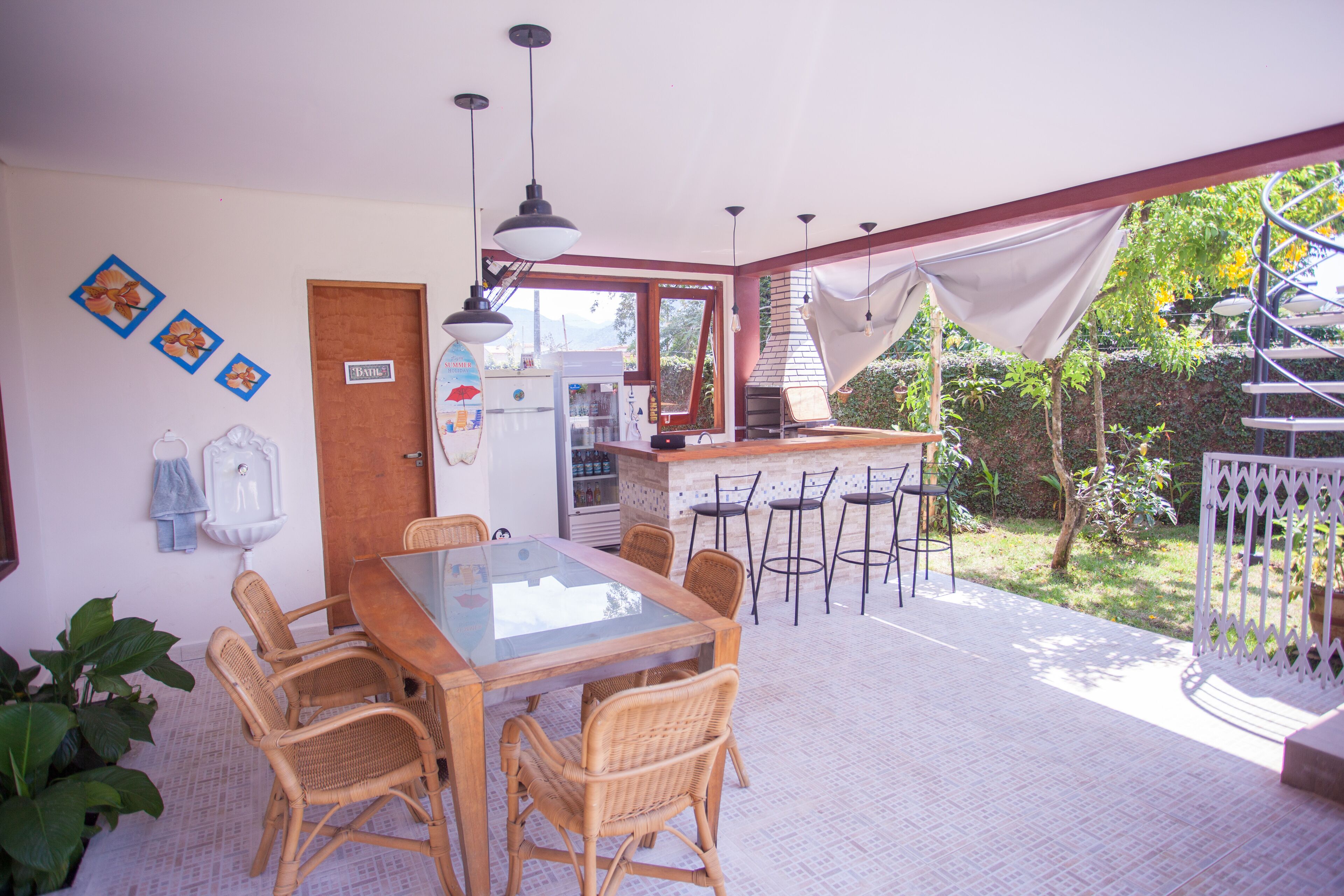A dining area with a glass-top table and wicker chairs, a kitchen with a brick stove, and a spiral staircase leading to an outdoor area.