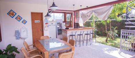 A dining area with a glass-top table and wicker chairs, a kitchen with a brick stove, and a spiral staircase leading to an outdoor area.