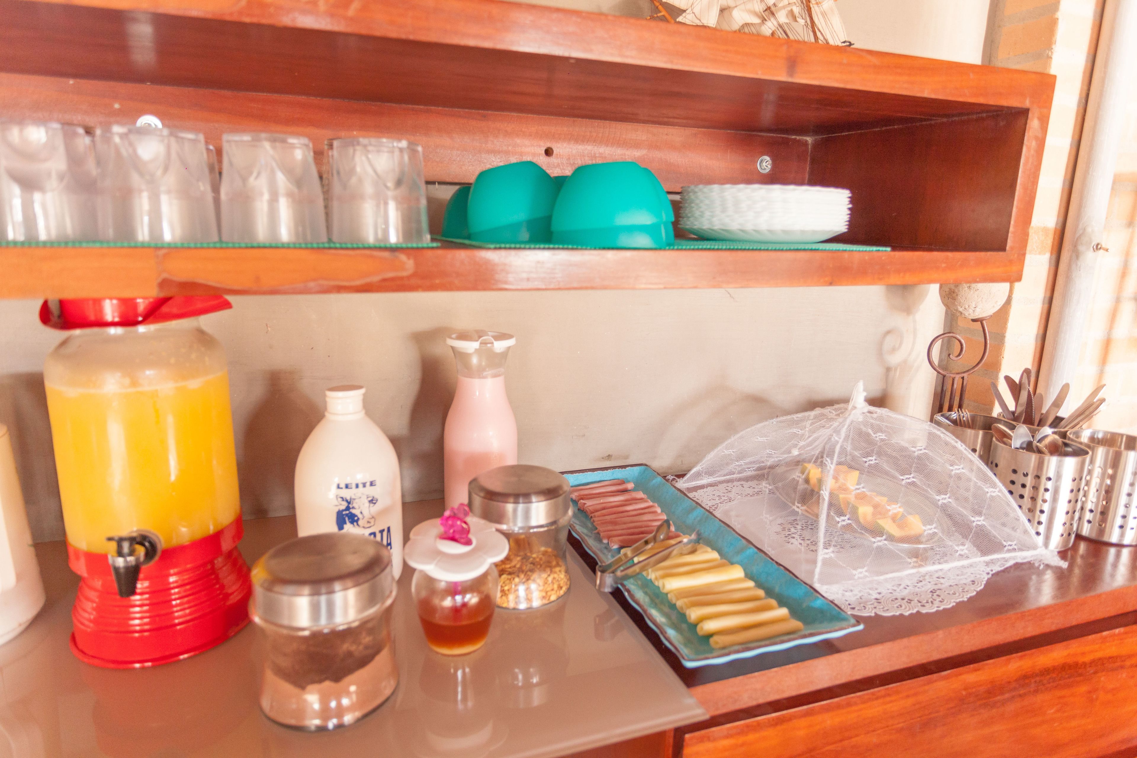 A kitchen counter with a juice dispenser, a bottle of milk, a jar of honey, a plate of pastries, and a coffee maker.