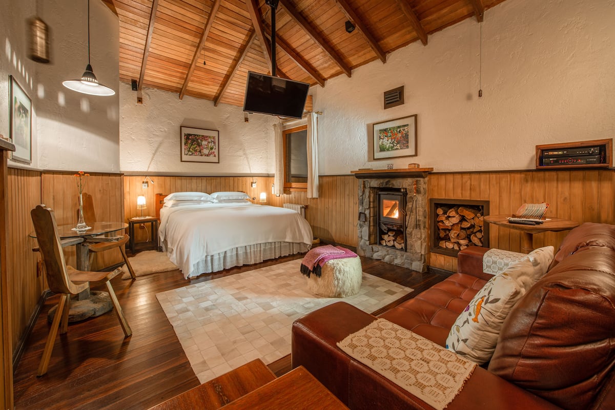 A cozy room with a bed, a fireplace, a wooden ceiling, and a television.