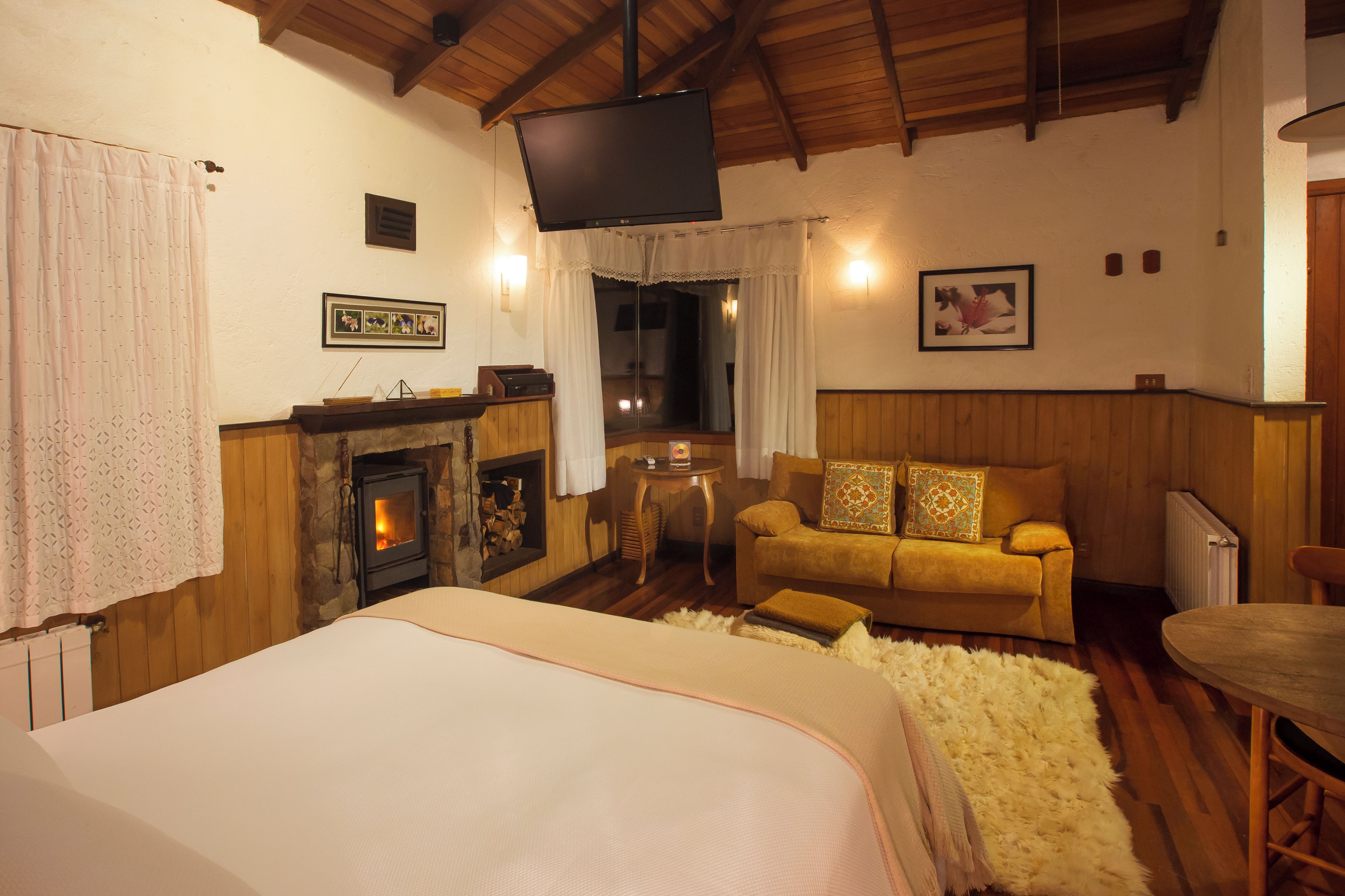 A cozy room with a large bed, a fireplace, a sofa, and a television mounted on the wall.
