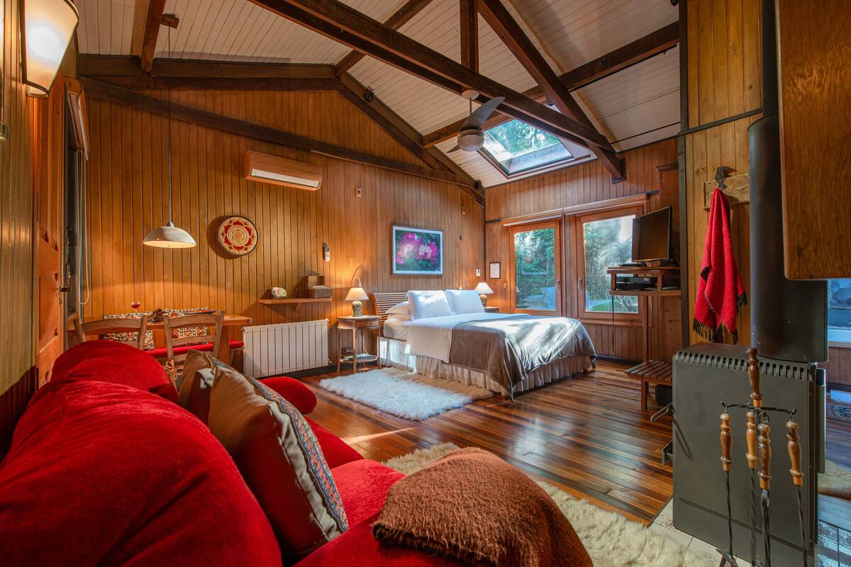 A cozy room with a bed, a red sofa, a wooden floor, and a large window.