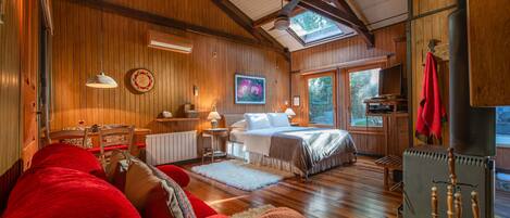 Une pièce confortable avec un lit, un canapé rouge, un plancher en bois et une grande fenêtre.