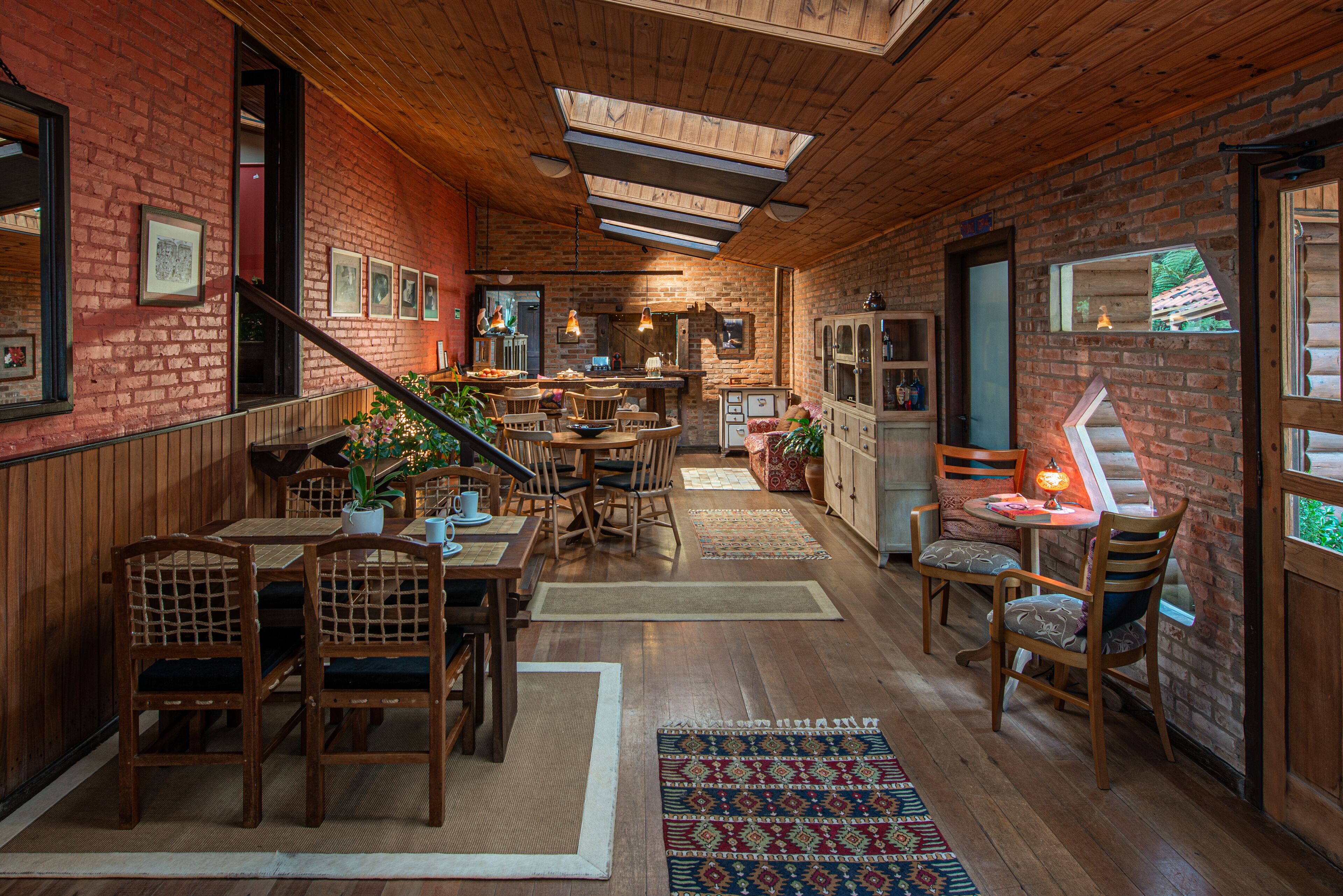 A cozy, rustic interior with wooden floors, brick walls, and a variety of seating areas including tables and chairs.