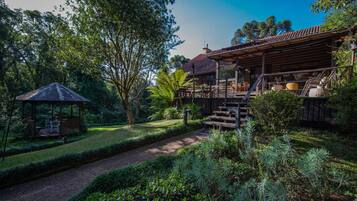 Una casa de madera con un porche cubierto, un pabellón y un jardín bien cuidado con diversas plantas y un sendero de grava.