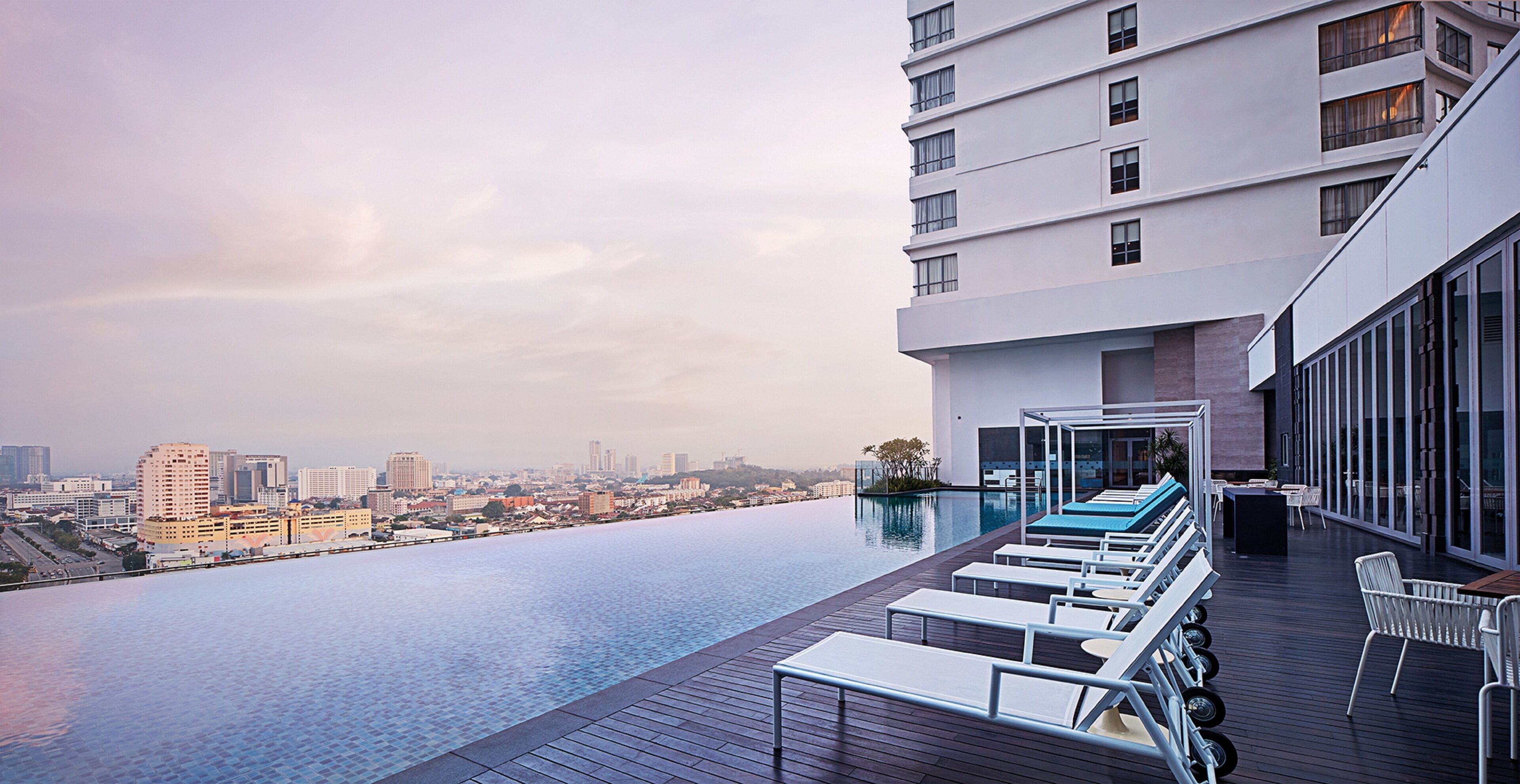A modern hotel with a rooftop infinity pool overlooking a cityscape.