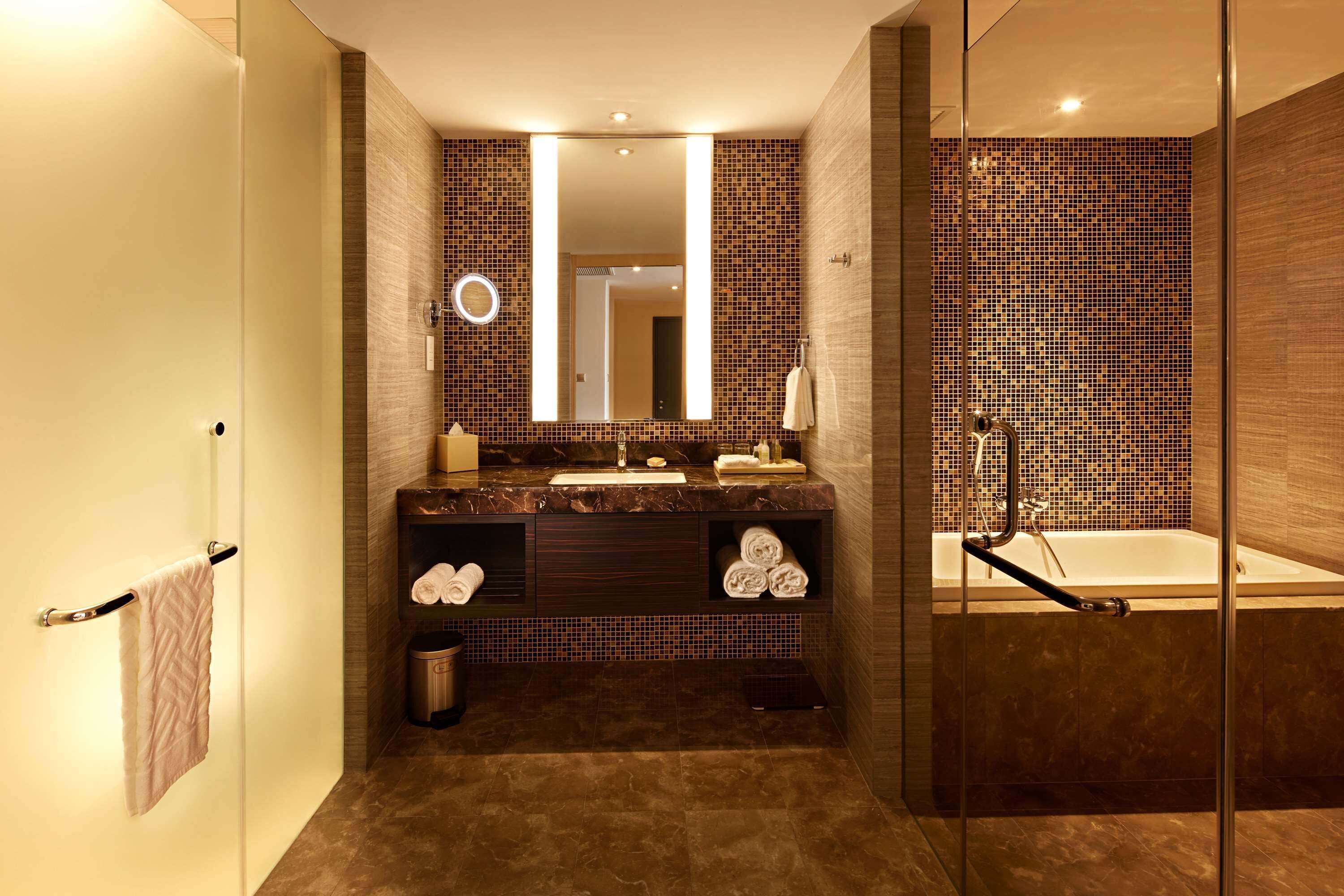 A modern bathroom with a large mirror, a bathtub, and a vanity with a sink and towel rack.