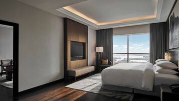 A modern hotel room with a large bed, a TV, a desk, and a view of the cityscape.