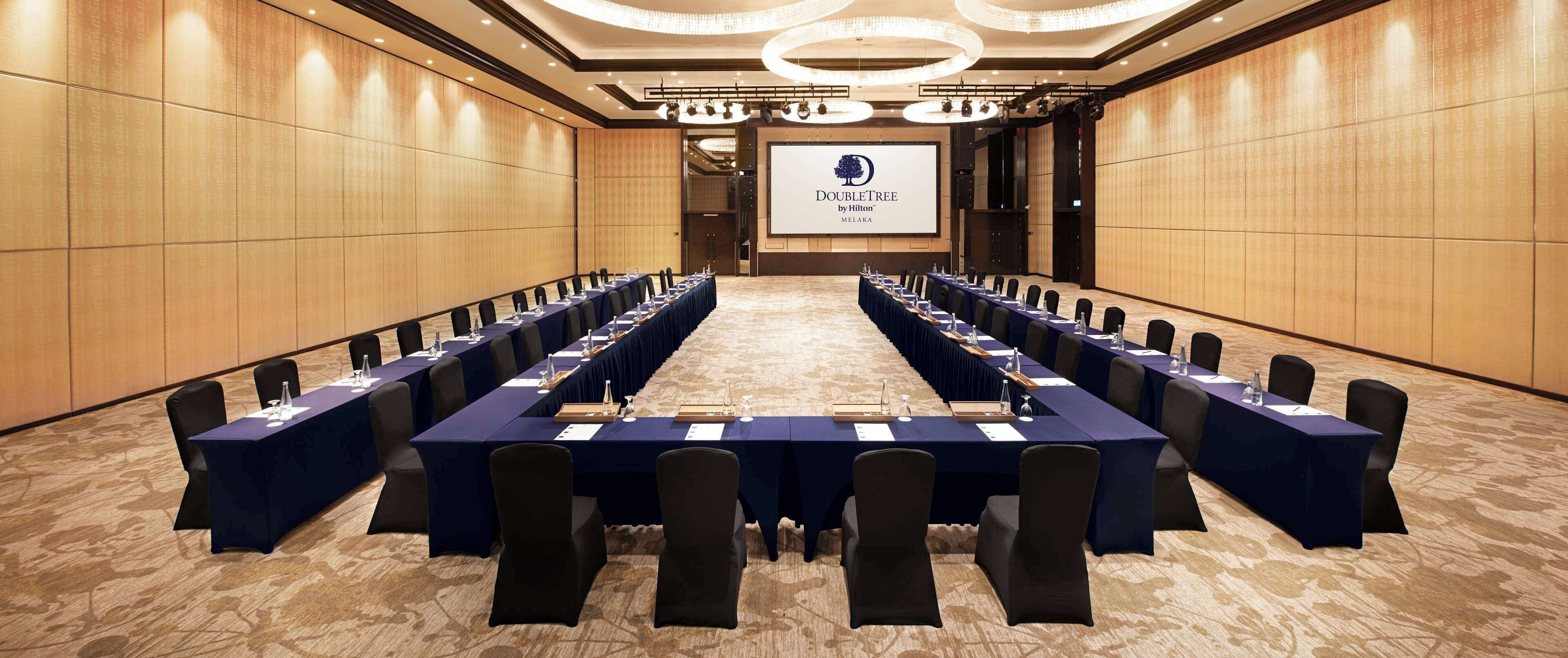 A conference room with a long table, black chairs, and a screen displaying the DoubleTree by Hilton logo.