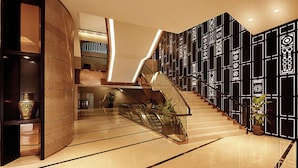 Un hall d’hôtel moderne avec un mur incurvé, un escalier en verre et un motif décoratif sur le mur.