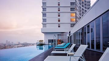 Un hôtel moderne doté d’une piscine à débordement sur le toit, de chaises longues et offrant une vue sur la ville.