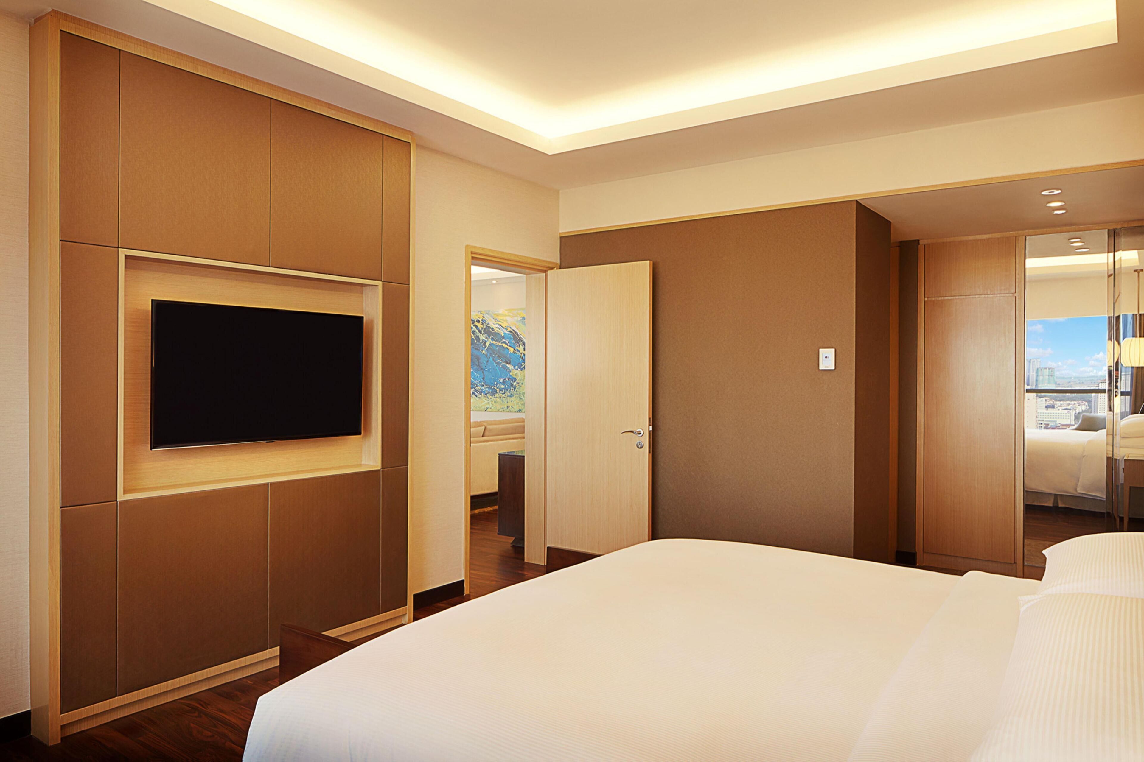A hotel room with a large bed, a flat-screen TV mounted on the wall, and a door leading to a balcony with a view.