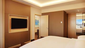 A hotel room with a large bed, a flat-screen TV mounted on the wall, and a door leading to a balcony with a view.
