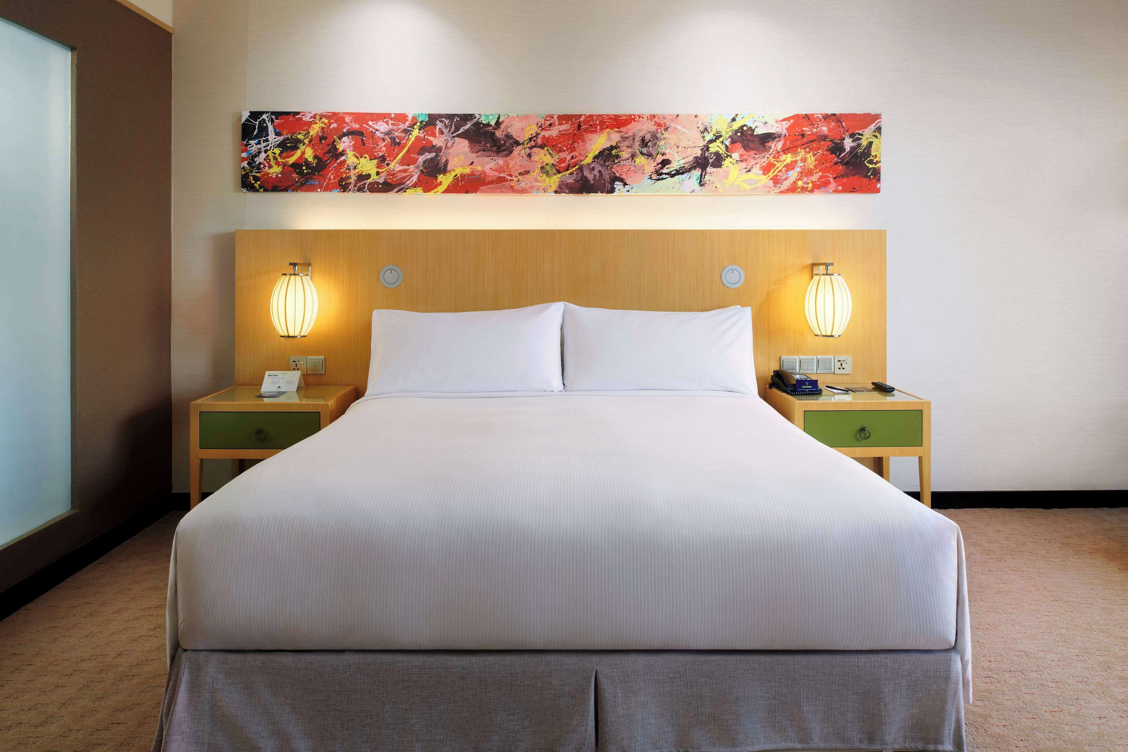 Una habitación de hotel con una cama grande, dos mesitas de noche, una obra de arte en la pared y una ventana.