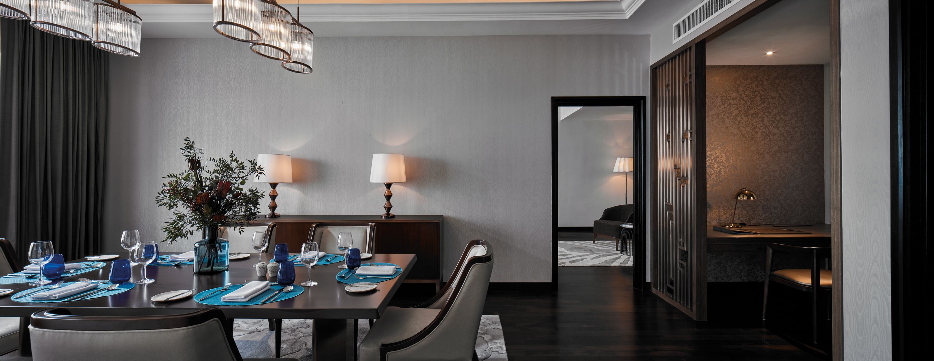 A modern dining area with a dark wood table set for four, blue placemats, and two table lamps.