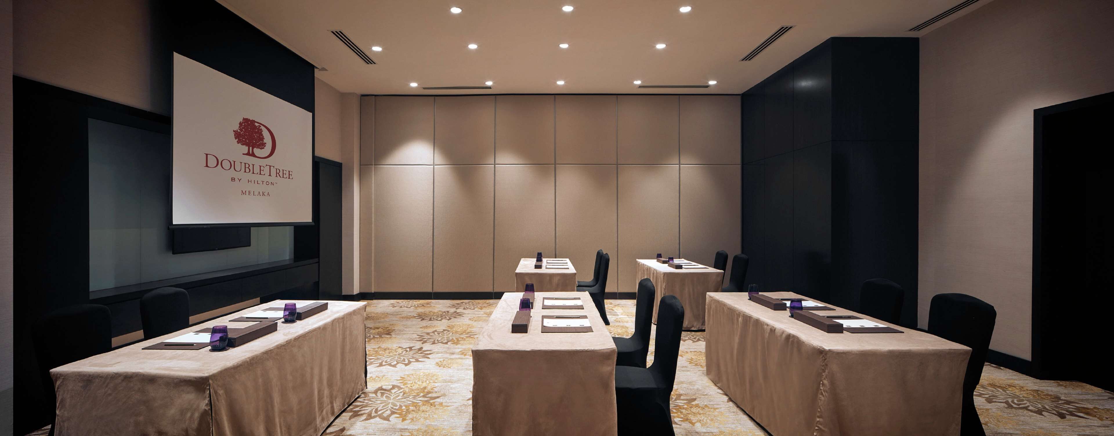A conference room with tables, chairs, and a presentation screen displaying the DoubleTree logo.