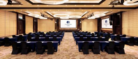 A conference room with rows of tables and chairs, a large screen at the front, and a chandelier.