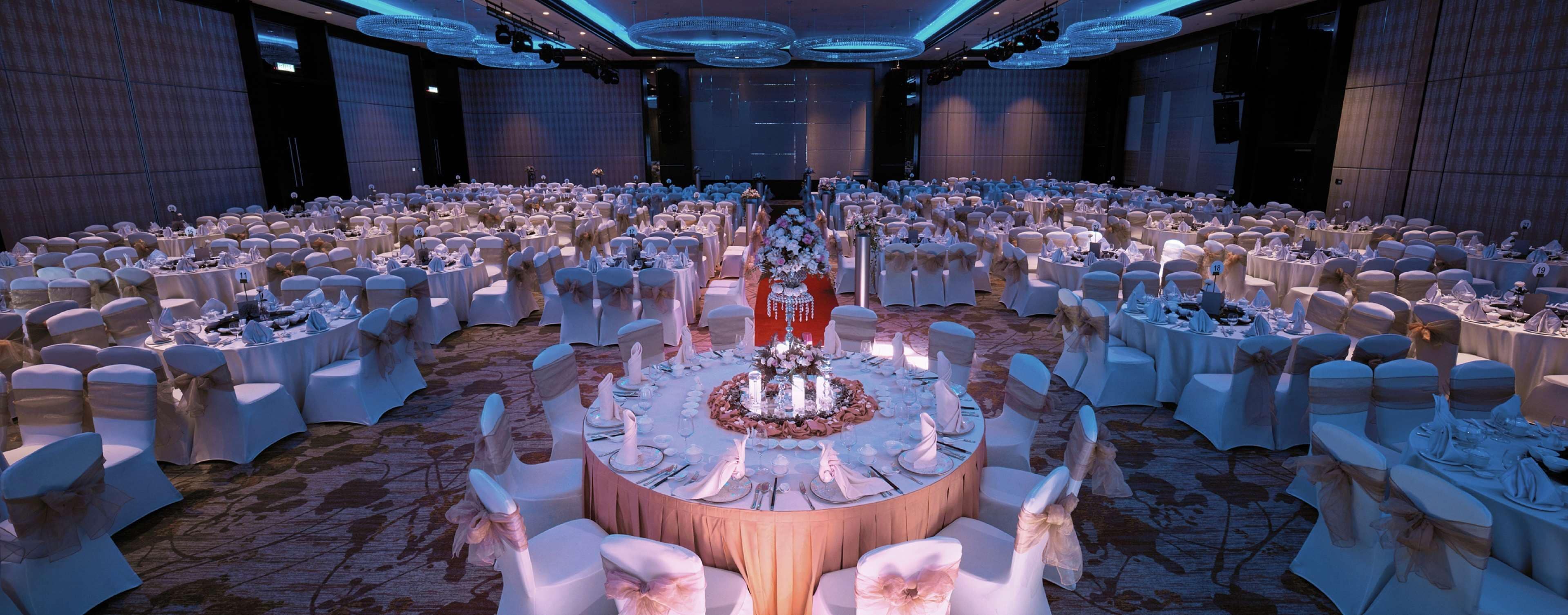Une grande salle de banquet avec des tables rondes et des chaises blanches, disposées en arc de cercle.