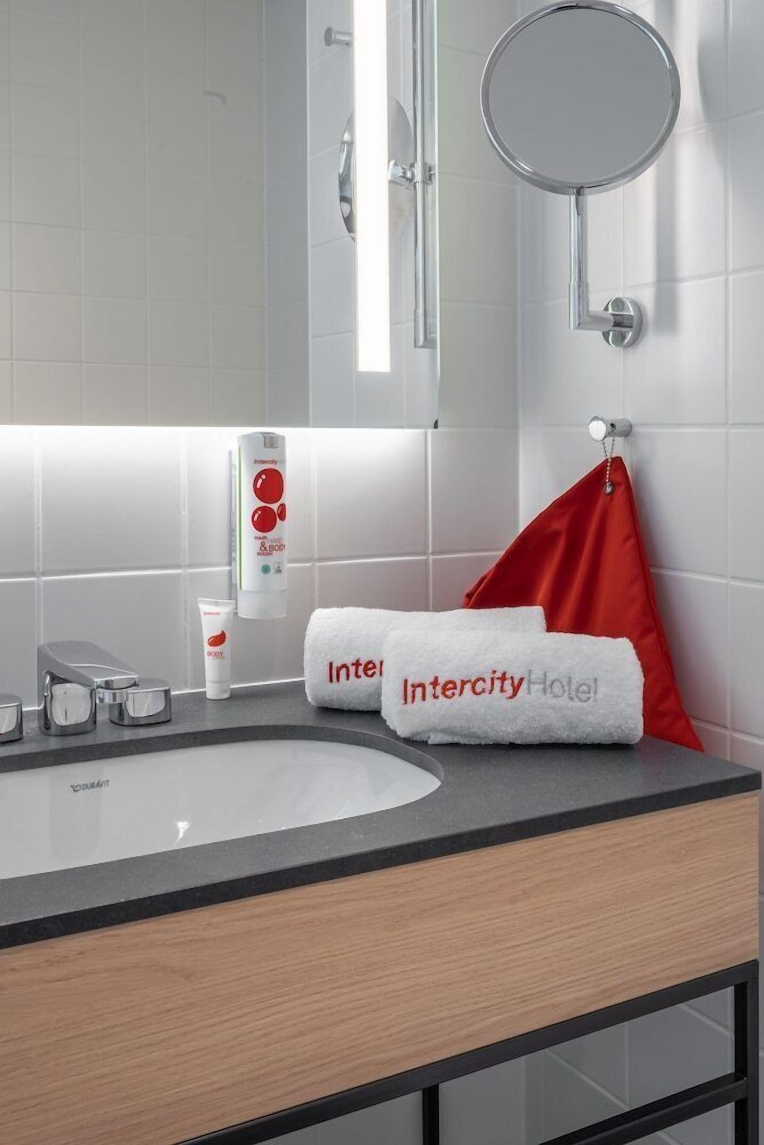 A modern bathroom with a white sink, a mirror, and toiletries.