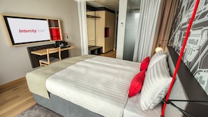A modern hotel room with a bed, a desk, a TV screen displaying "Intercity Hotel," and a cityscape wall art. - IntercityHotel Duisburg (Duisburg)