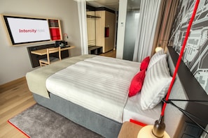 A modern hotel room with a bed, a desk, a TV screen displaying "Intercity Hotel," and a cityscape wall art. - IntercityHotel Duisburg (Duisburg)