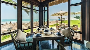 A dining area with a view of the beach, large windows, and outdoor umbrellas. - The Anam Cam Ranh (Cam Lam)